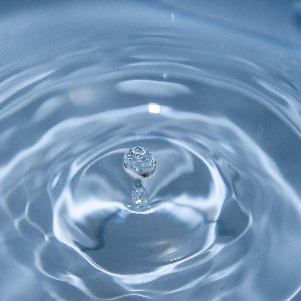 A single water droplet rippling in a glass of water